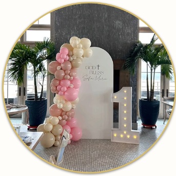 Pink and ivory Communion balloons beside a personalized panel and illuminated cross