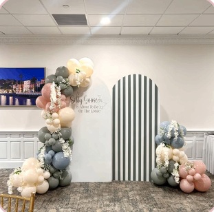 Muted pink and blue baby shower balloons beside a striped arched panel