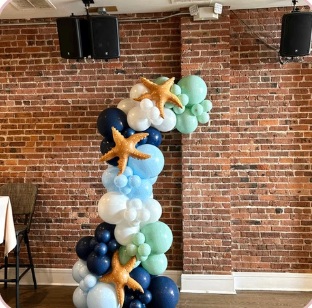 Blue and seafoam balloon column with starfish beside a brick wall