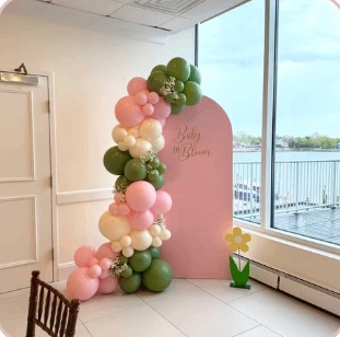 Pink and olive baby shower balloons beside a window overlooking the water