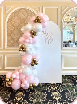 Pink, white and gold balloons beside an arched celebration backdrop
