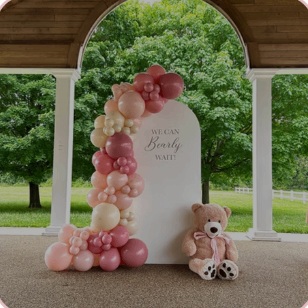 Pink and ivory outdoor baby shower backdrop with a teddy bear