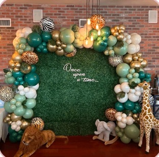 Safari-inspired baby shower arch with green and gold balloons and animal props