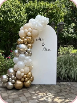 White, gold and silver balloon garland beside a garden wedding backdrop